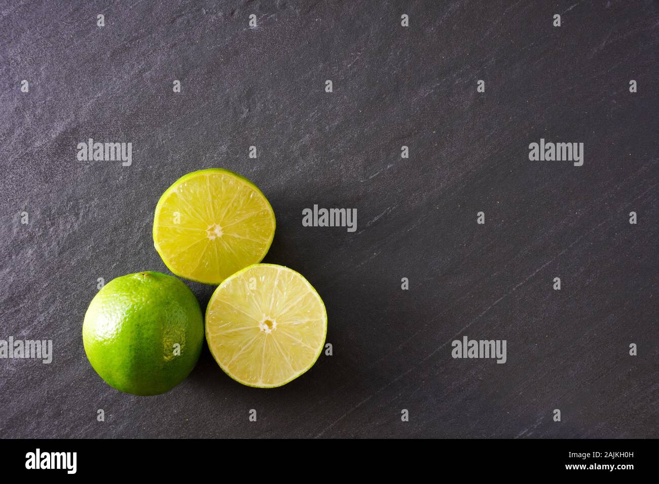 Two halves of a lime next to a whole lime on a black slate background with copy space on the right Stock Photo