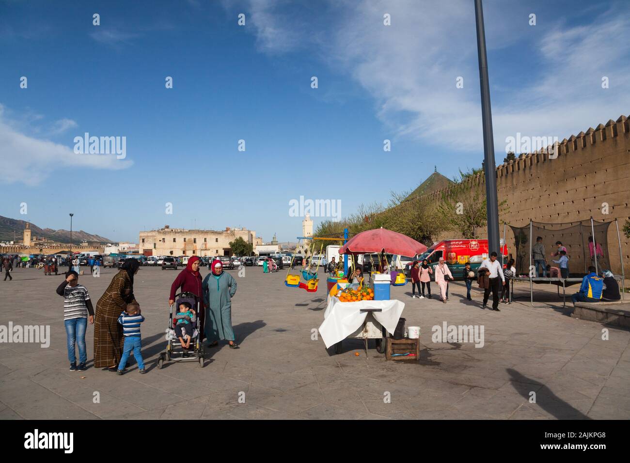 Traditionally dressed women with children, stall with oranges and children playing on carousel and  trampoline on Place Boujloud in Fes (Fez), Morocco Stock Photo