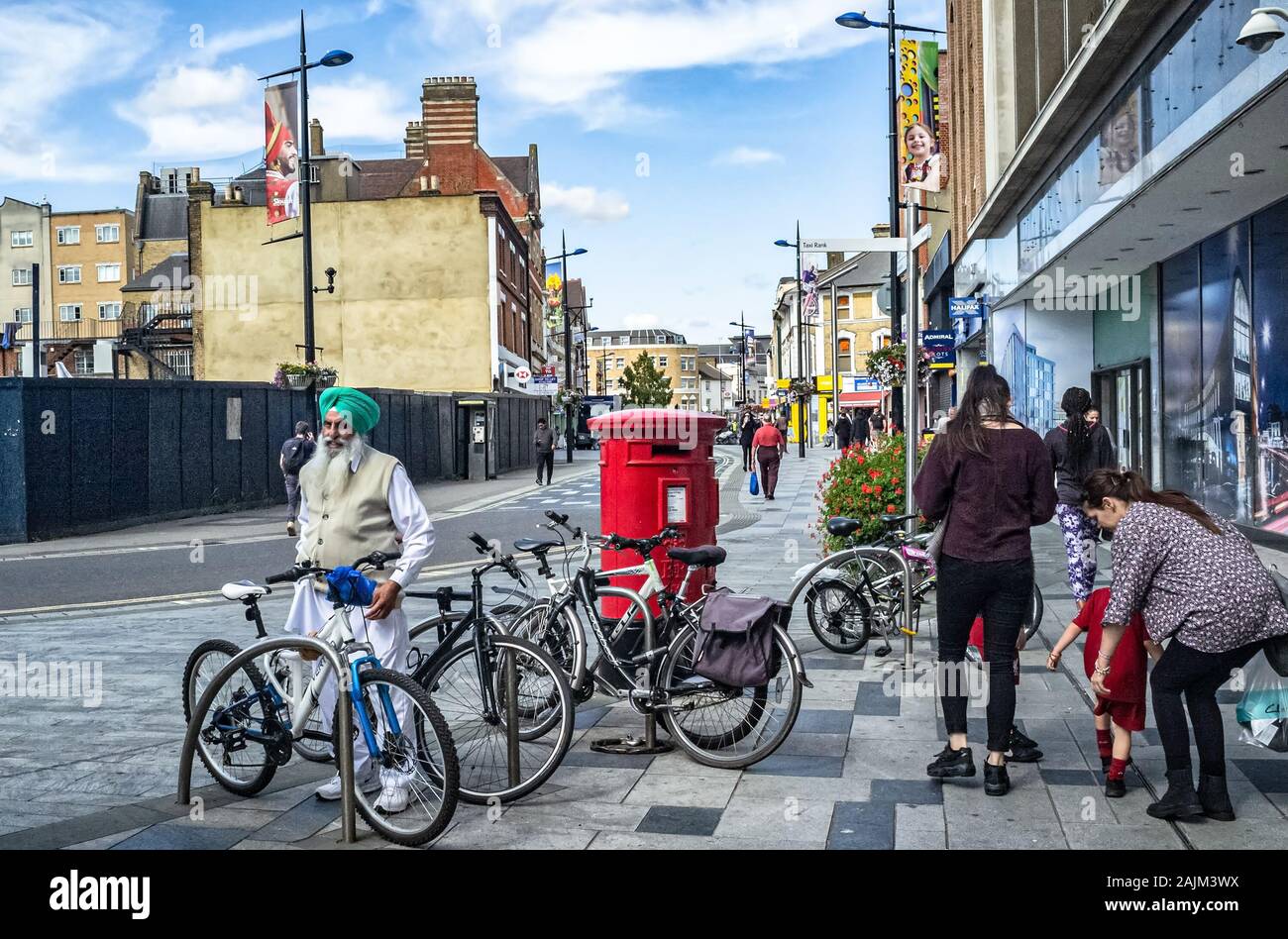Sikh man (age 60's) in traditional clothes and wearing a green turban, parks his bicycle at a bike rack in Slough city centre (Berkshire, UK) Stock Photo