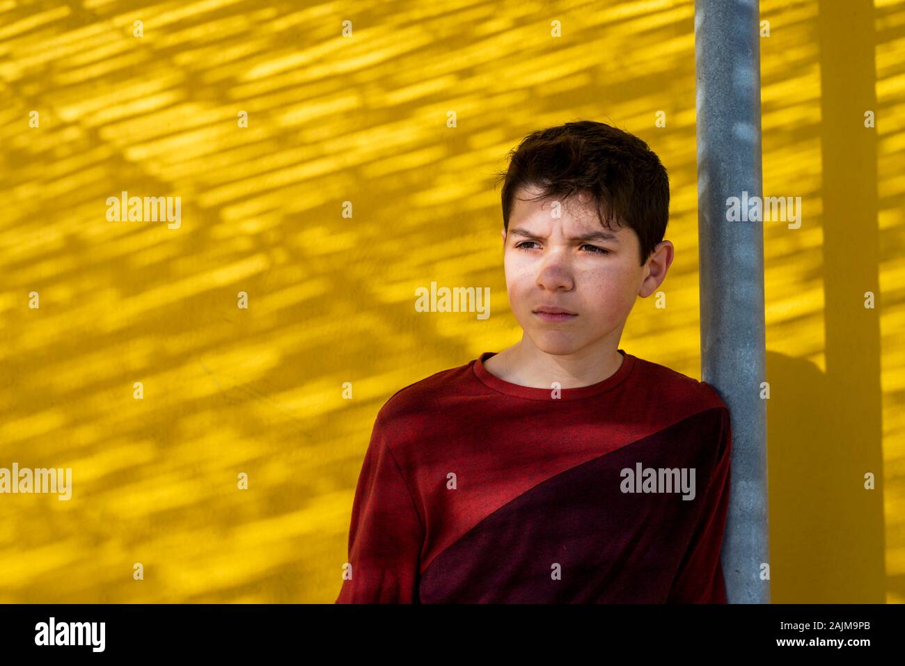 Portrait cheerful teen leaning against yellow wall, looking away Stock Photo