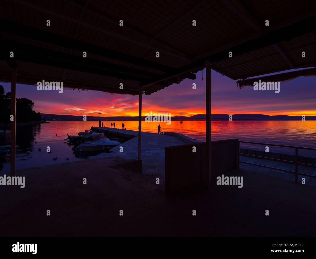 Fishermen before sunset scenery in small harbor in Malinska in Croatia framed by house roof Stock Photo