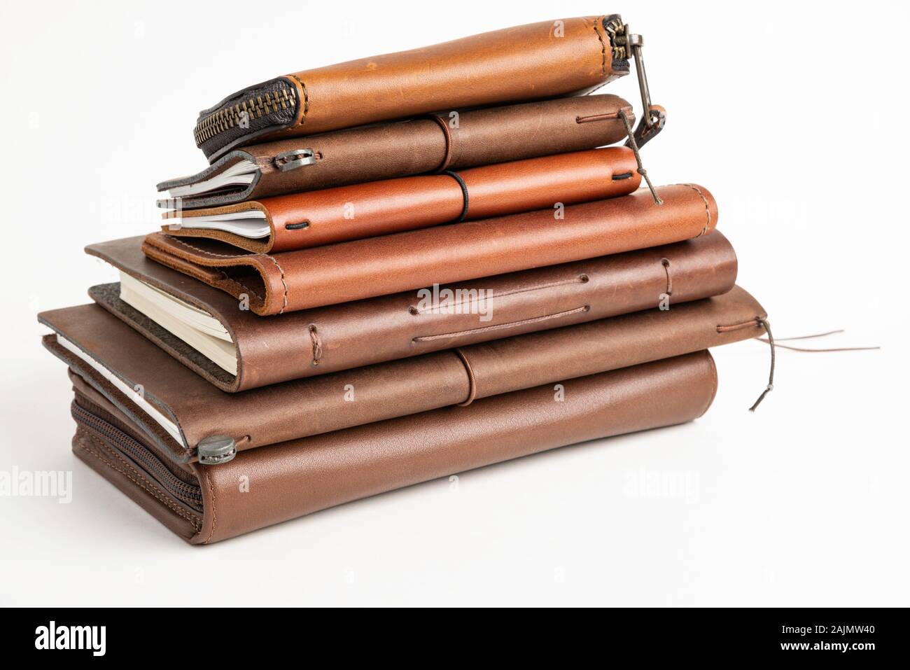 A stack of leather-bound journals, notebooks, cases, and wallets set on a plain white background. Stock Photo