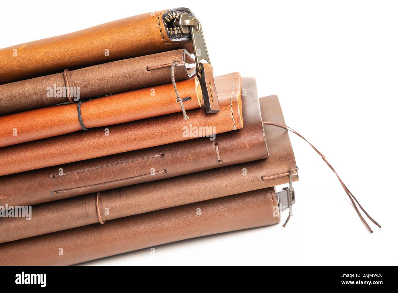 A stack of leather-bound journals, notebooks, cases, and wallets set on a plain white background. Stock Photo