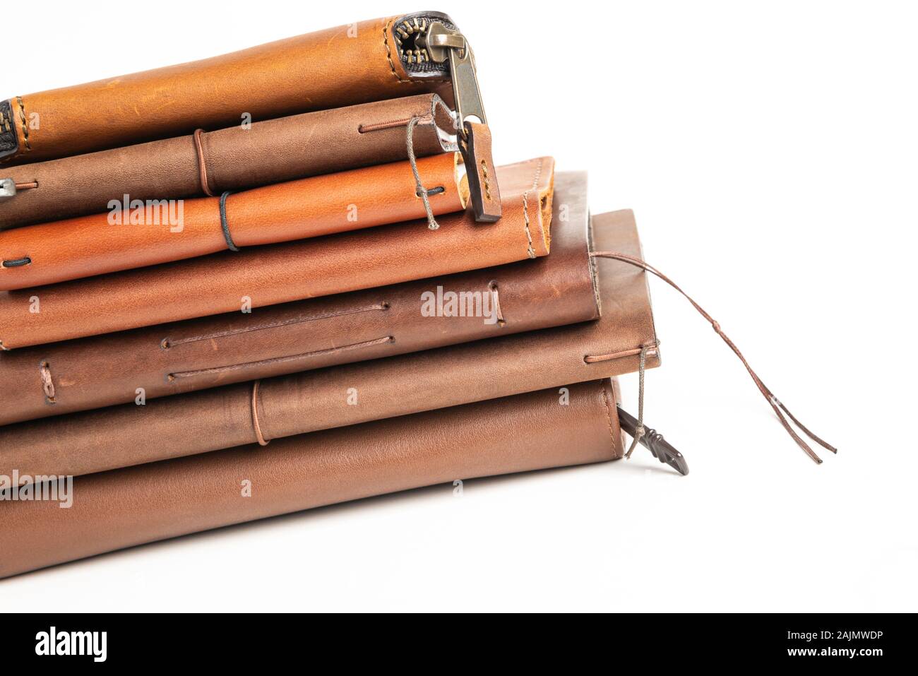 A stack of leather-bound journals, notebooks, cases, and wallets set on a plain white background. Stock Photo