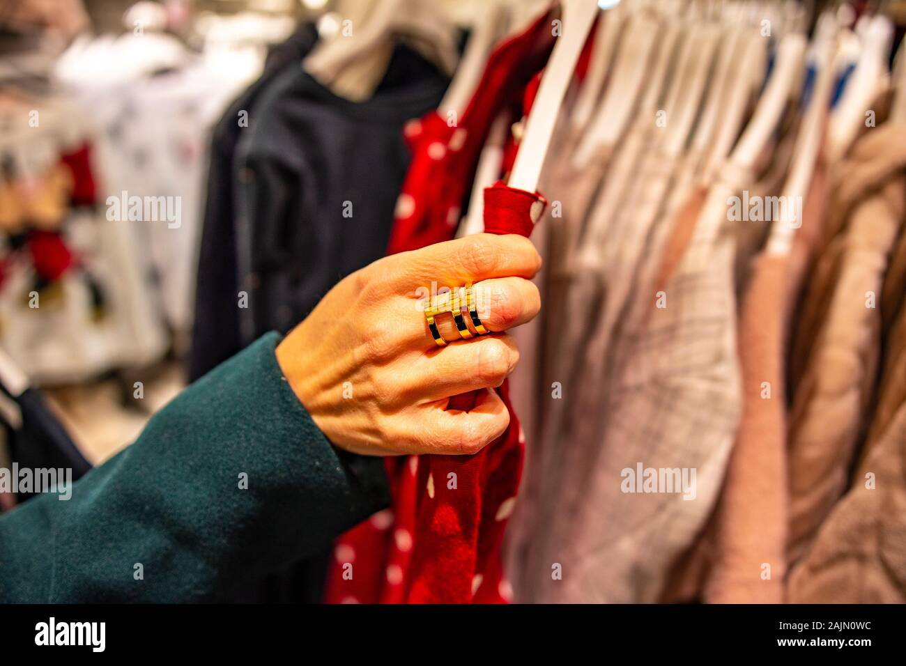 Modern woman shopping in fashion mall, choosing new clothes, looking through hangers with different casual colorful garments on hangers Stock Photo