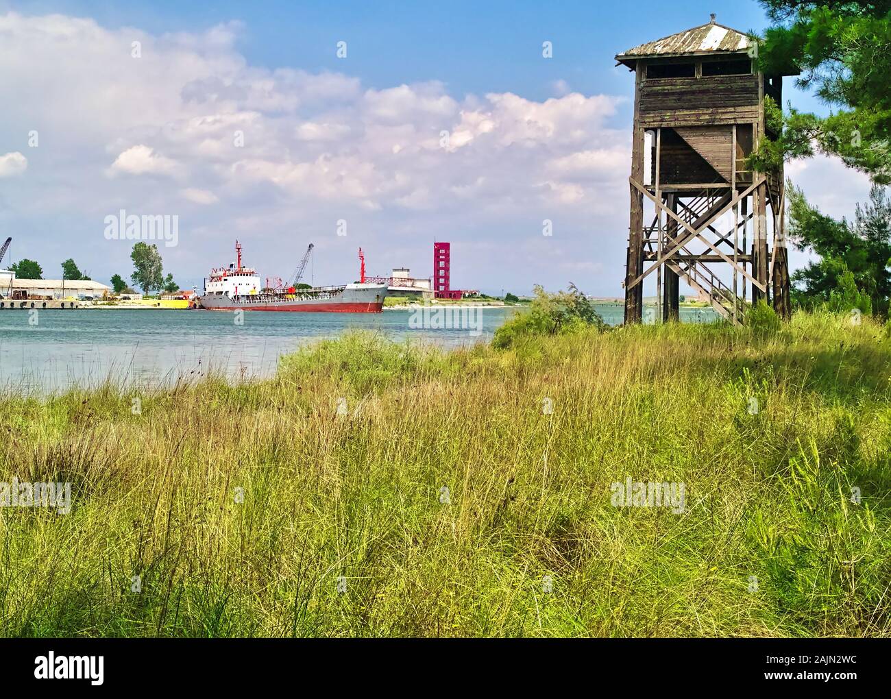 Wooden bird watch tower and port with commercial ships  and cranes. Grass and sky with clouds. Stock Photo