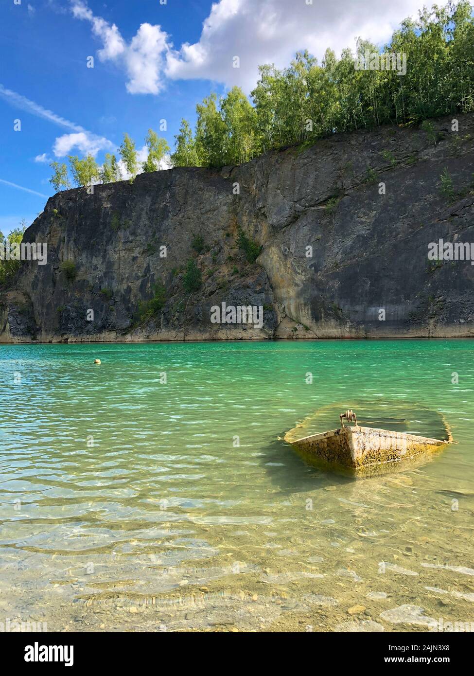 Abandoned boat in flooded quarry with blue crystal water. Diver site with fresh blue and clean water for divers Little abandoned boat sink in lake. Floreffe, Belgium. Stock Photo