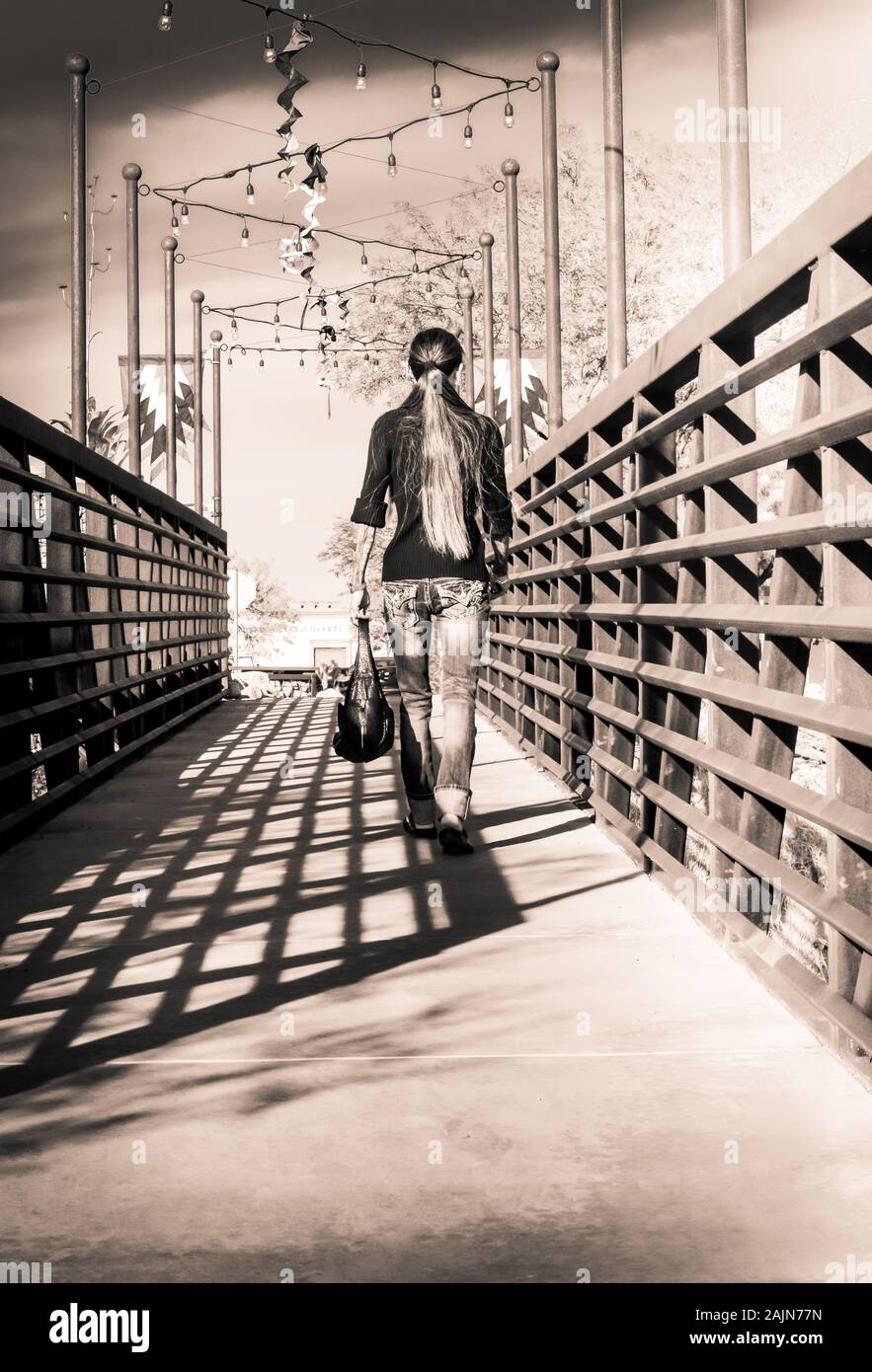 Rear view of hipster woman with tattoo sleeves strolling across the modern, metal, industrial designed pedestrian walkway in Tubac, AZ Stock Photo