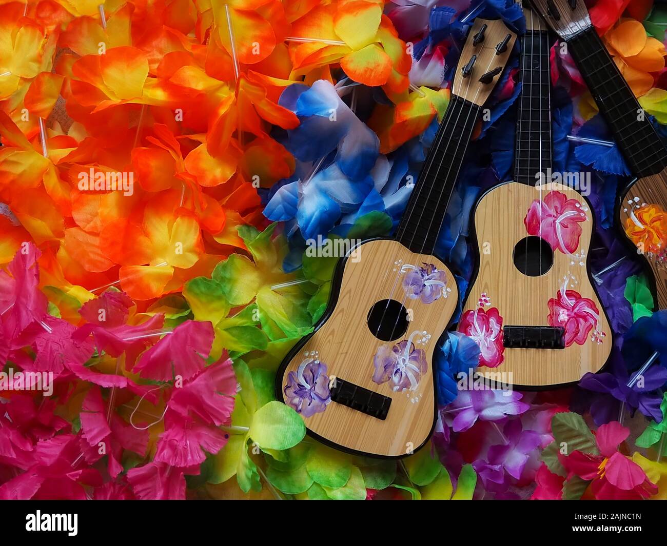 A collection of Hawaiian luau party decorations including two toy painted ukeleles on a bed of costume flower leis. Stock Photo