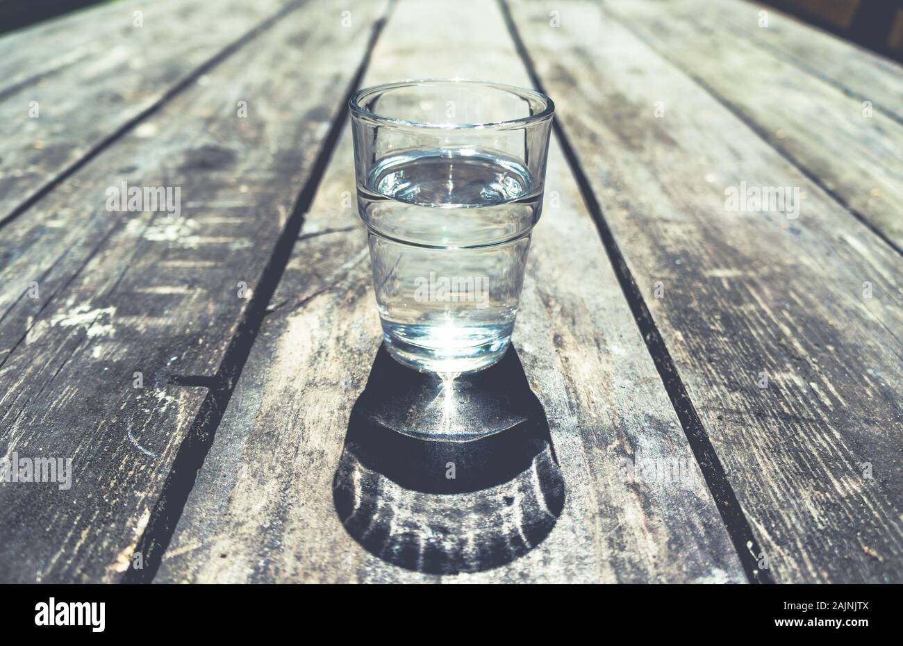Close-up of one glass of clear water standing in middle of rough wooden table Stock Photo