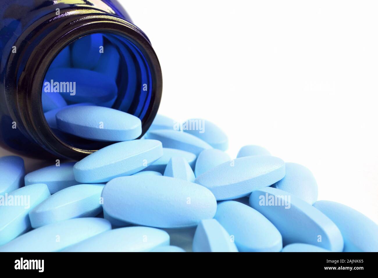 Light blue oval shaped pills scattered from deep blue glass bottle on white background with copy space Stock Photo