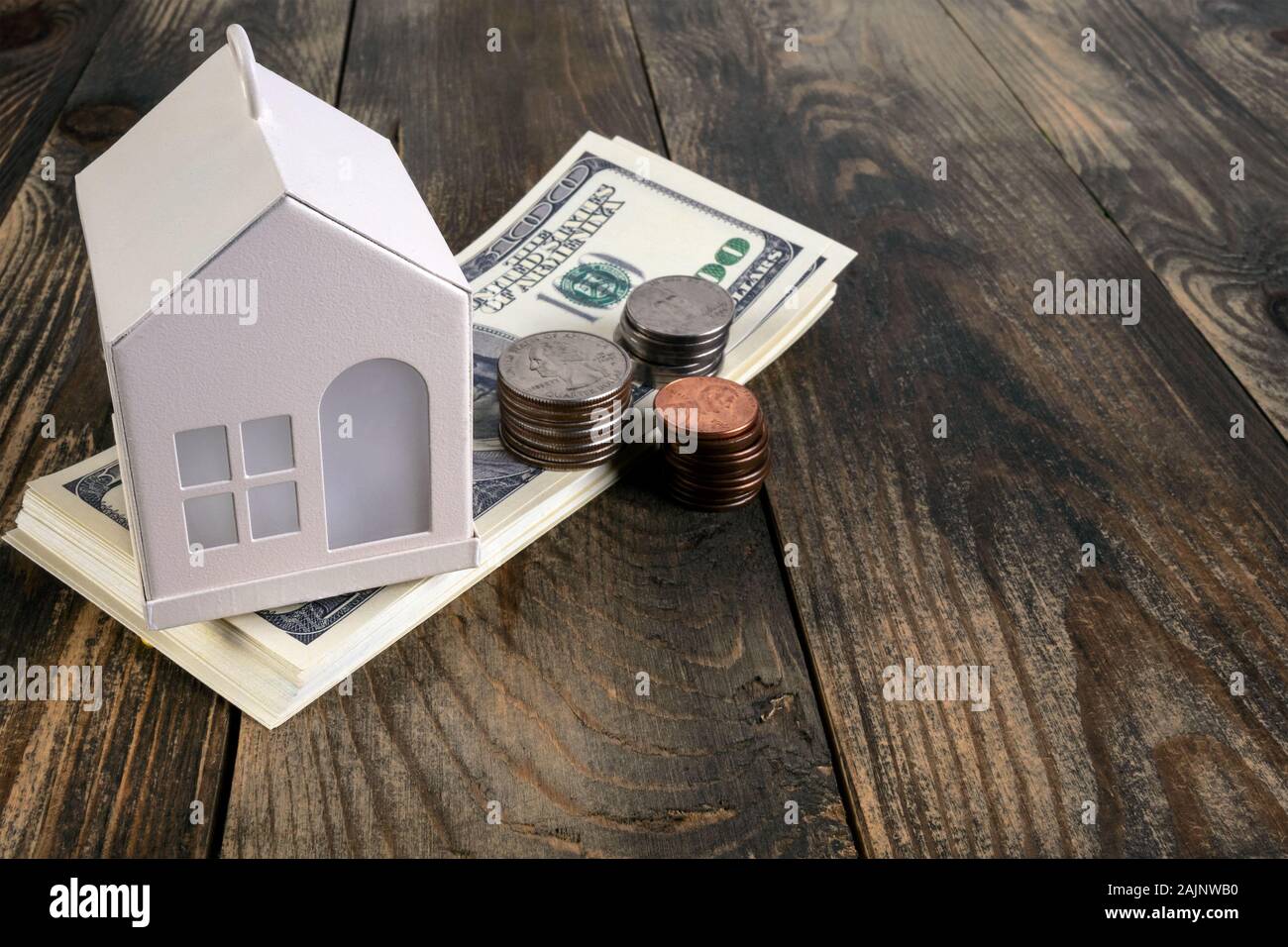 Mortgage or home ownership investment concept. Money and white toy house on table. US dollars and coins. Saving money for private house. Estate invest Stock Photo