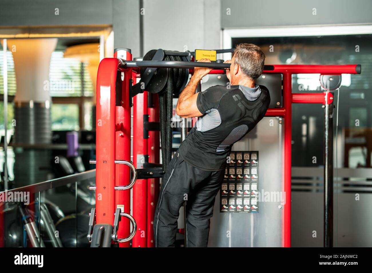 man strengthening his muscles by doing pull-up on horizontal bar in a fitness center. Stock Photo
