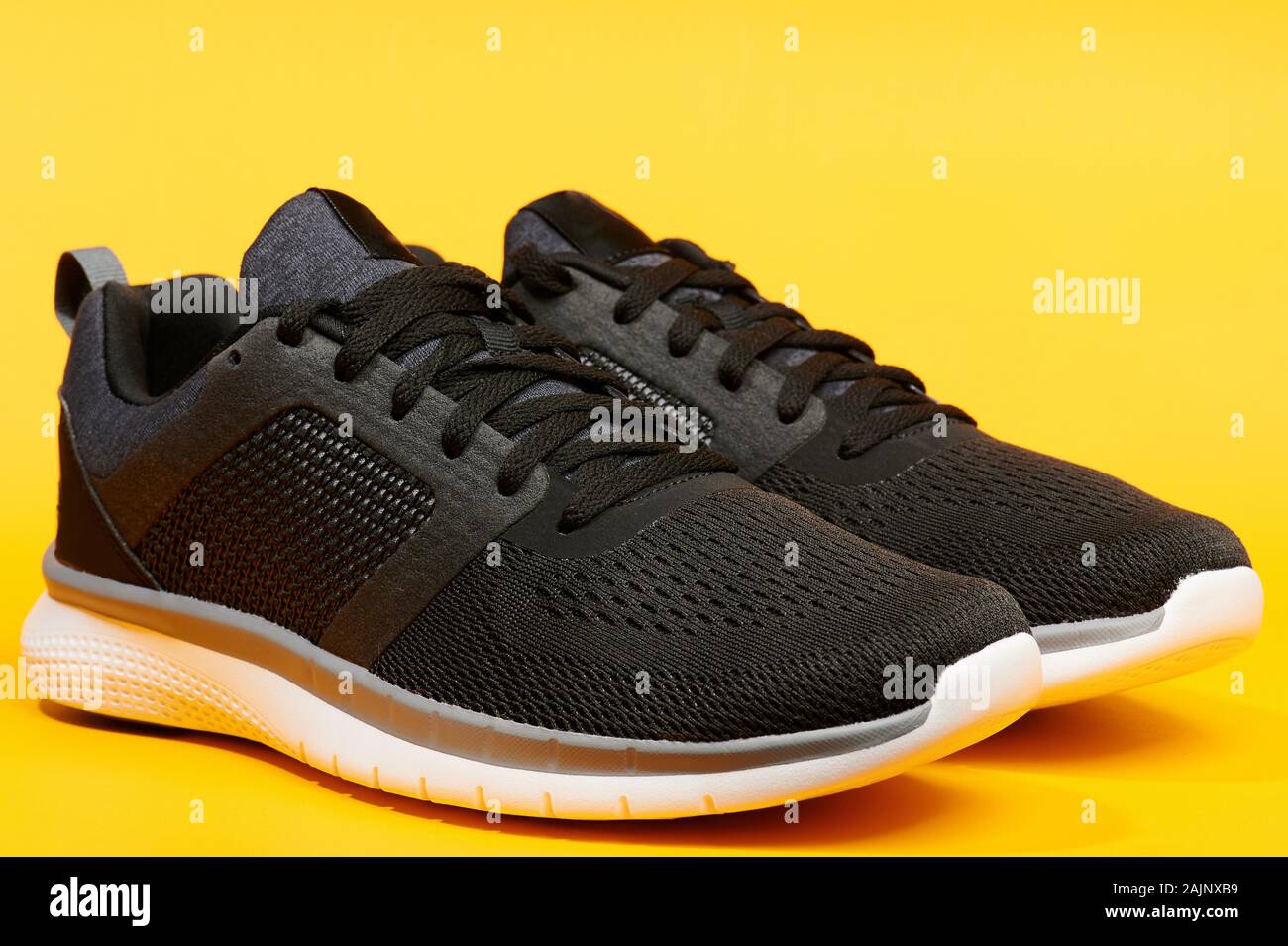 Pair of modern black running shoes on yellow bright background Stock Photo