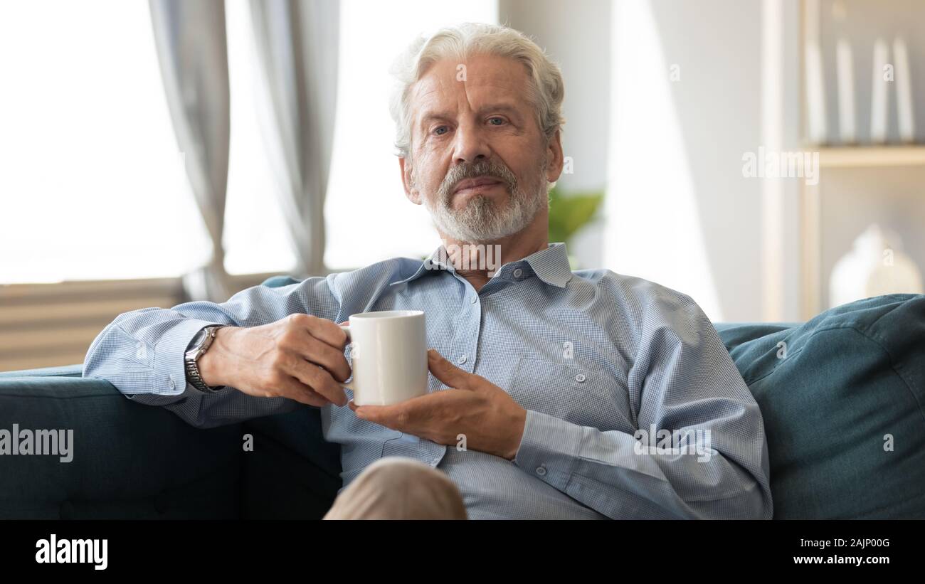 Elderly man sitting on couch holding cup looking at camera Stock Photo