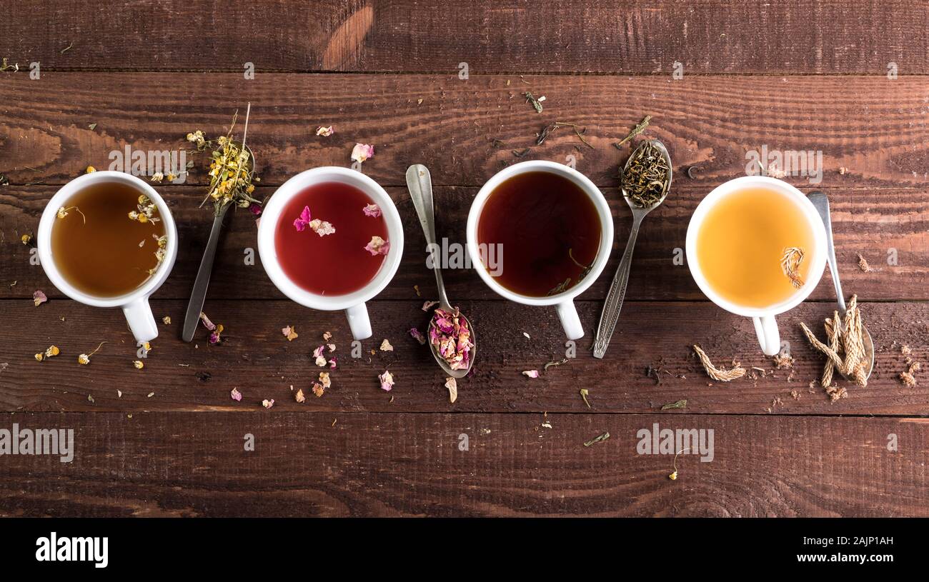 Assortment of cups of tee and dry tea in spoons a on wooden background. Top view with copy space. Stock Photo