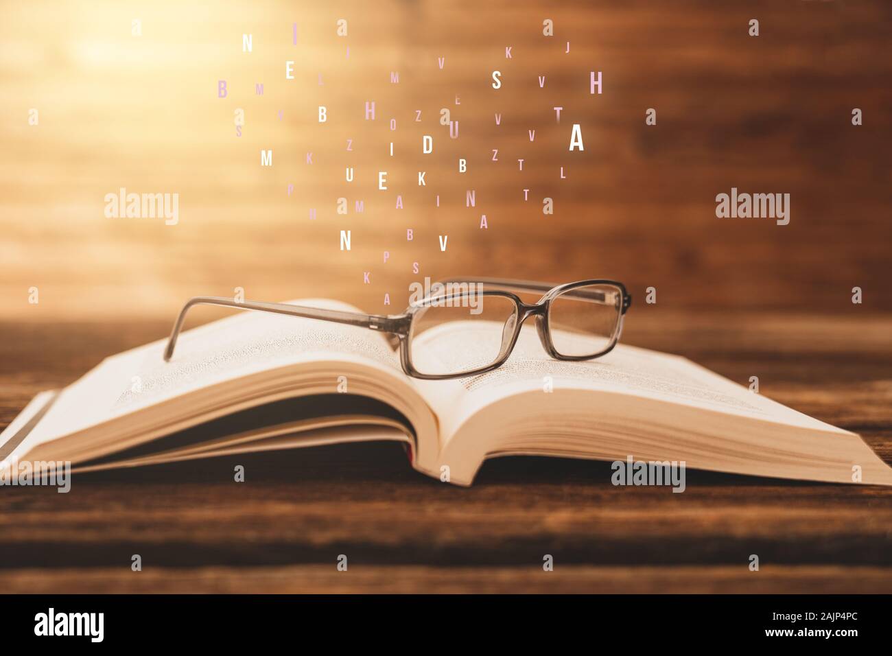 Eyeglasses on an open book and abstract letters on wooden table with vintage background Stock Photo