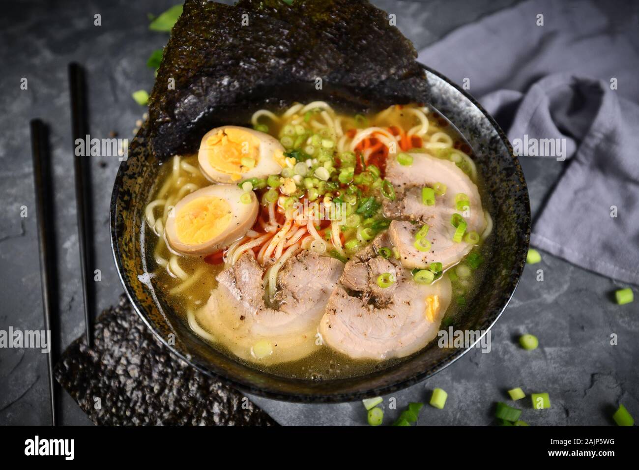 Homemade traditiona Japanese Ramen noudle soup with meat slices, egg and spring onions in dark bowl Stock Photo