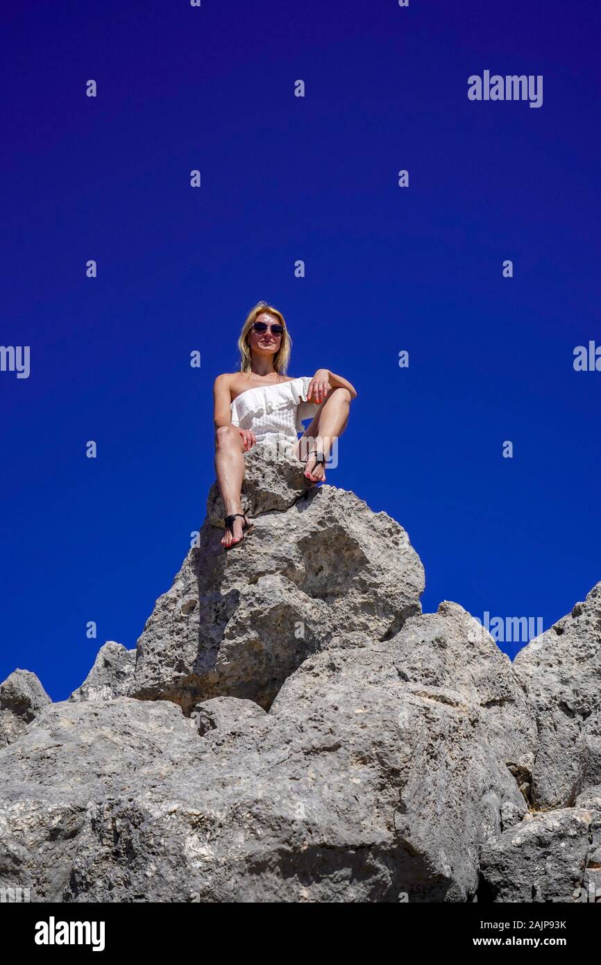 Blond female tourist admires the view while sitting on a rock on Aenos (Ainos) mountain on the Greek Island of Cephalonia, Ionian Sea, Greece with a b Stock Photo