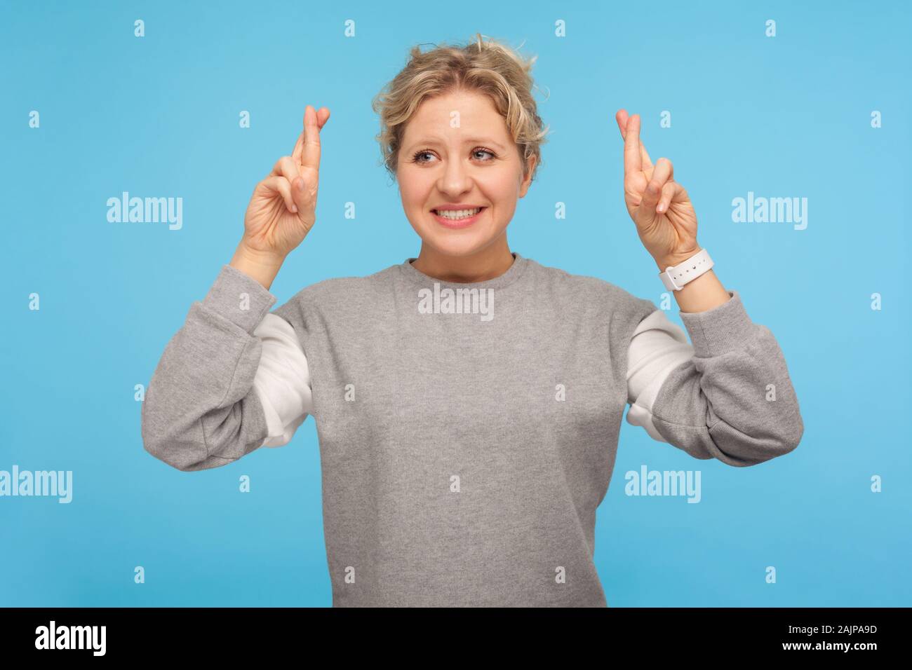 Need fortune. Positive woman with short hair in sweatshirt holding crossed fingers and wishing for good luck, having excited look, hoping for victory. Stock Photo