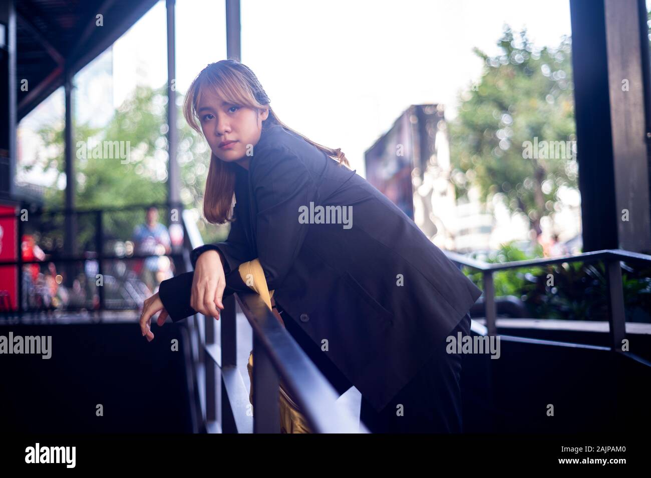 Blond hair woman with half-tied hair bend down herself on the handrail of the slope path in the shopping mall after work. Stock Photo