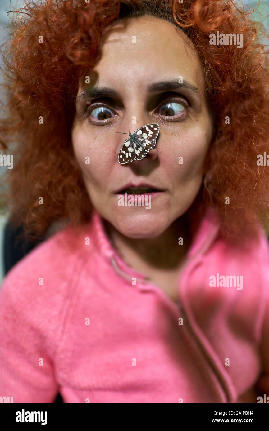 Funny portrait of a woman surprised by the butterfly landing on the tip of her nose Stock Photo