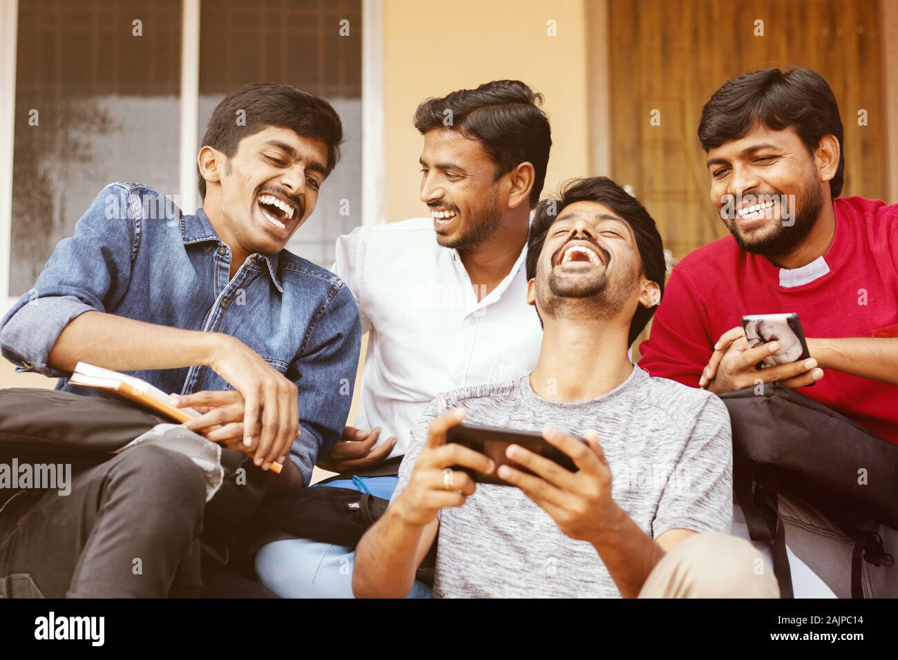 Group of happy young college students by looking at mobile phone laughing loudly at university campus - Millennials enjoying online video content or Stock Photo