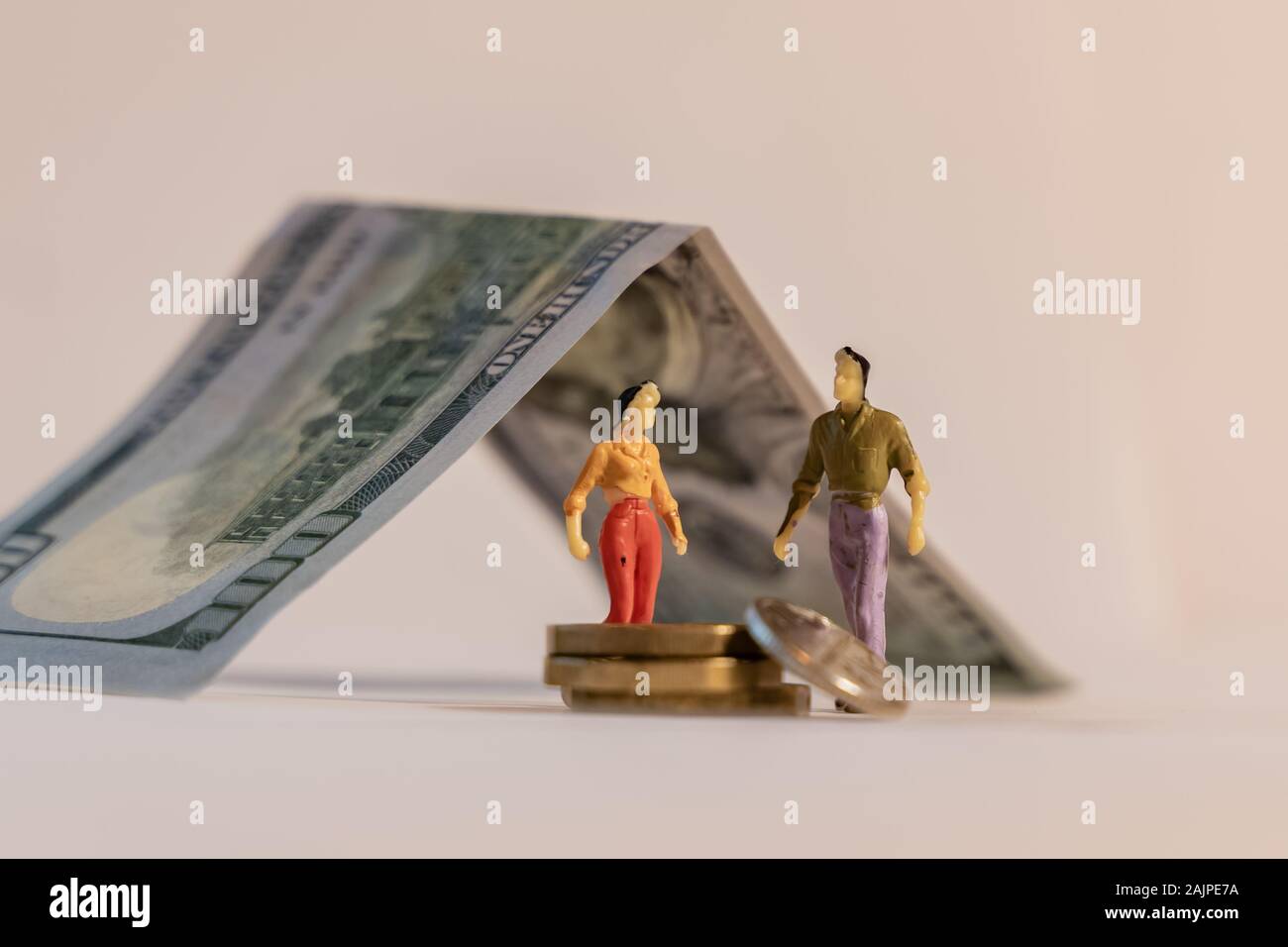 Miniature woman and man figure standing next to house made of dollar bill and counting coins. Shallow depth of field background. Family budget, mortga Stock Photo