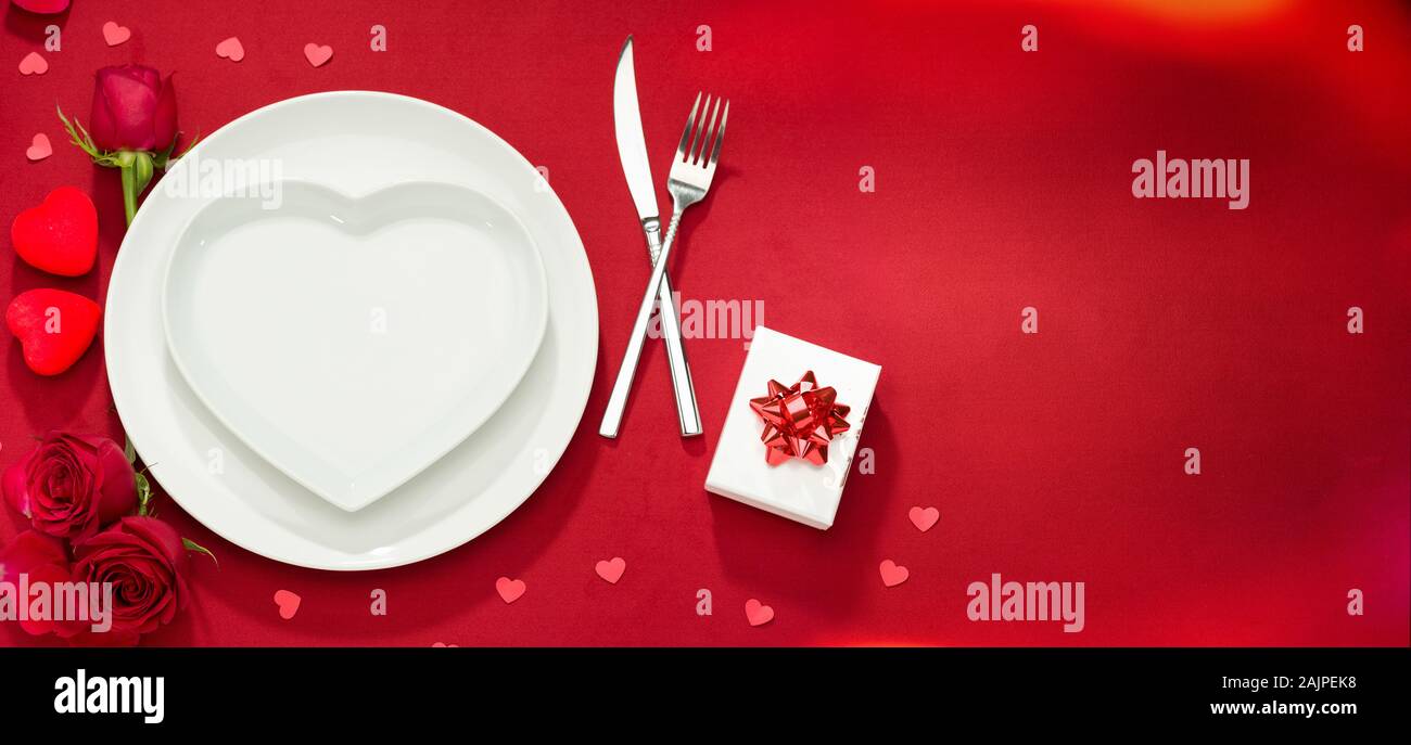 Valentine food background. Plate, fork, knife and roses on red cover Stock Photo