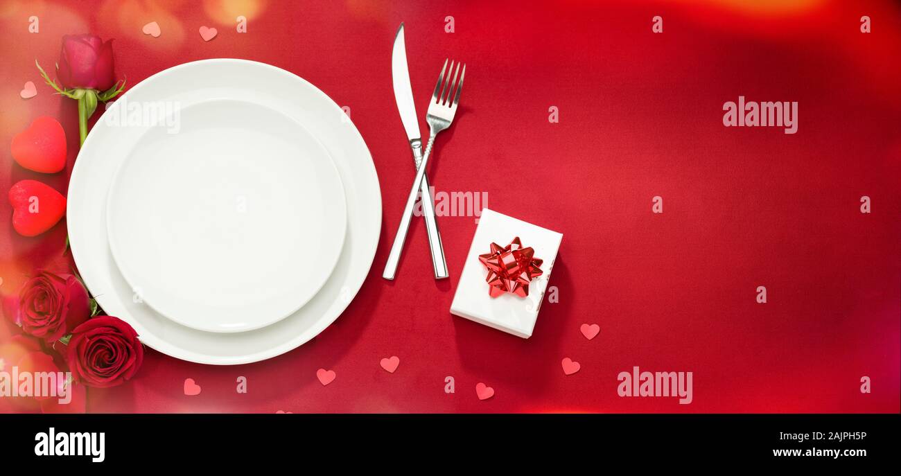 Valentine food background. Plate, fork, knife and roses on red cover Stock Photo