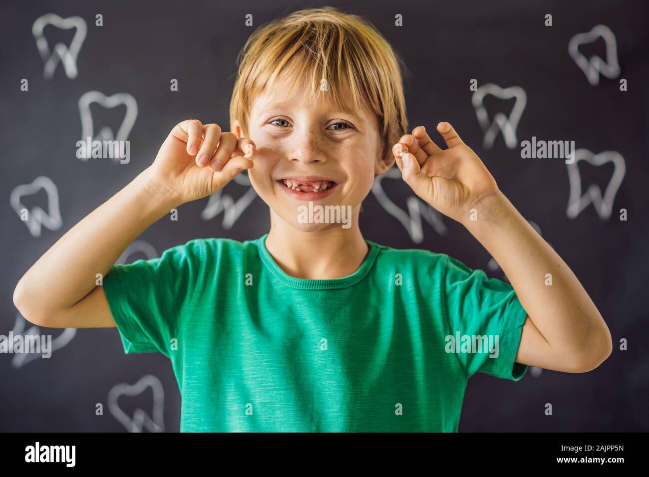 Litle caucasian boy holds a dropped milk tooth between his fingers and laughs looking into the camera Stock Photo