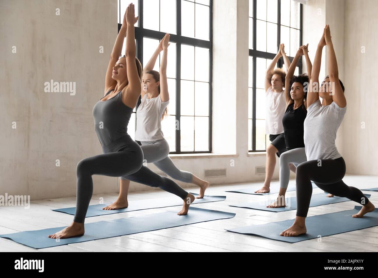 Diverse people practicing yoga, standing in Warrior one pose Stock Photo