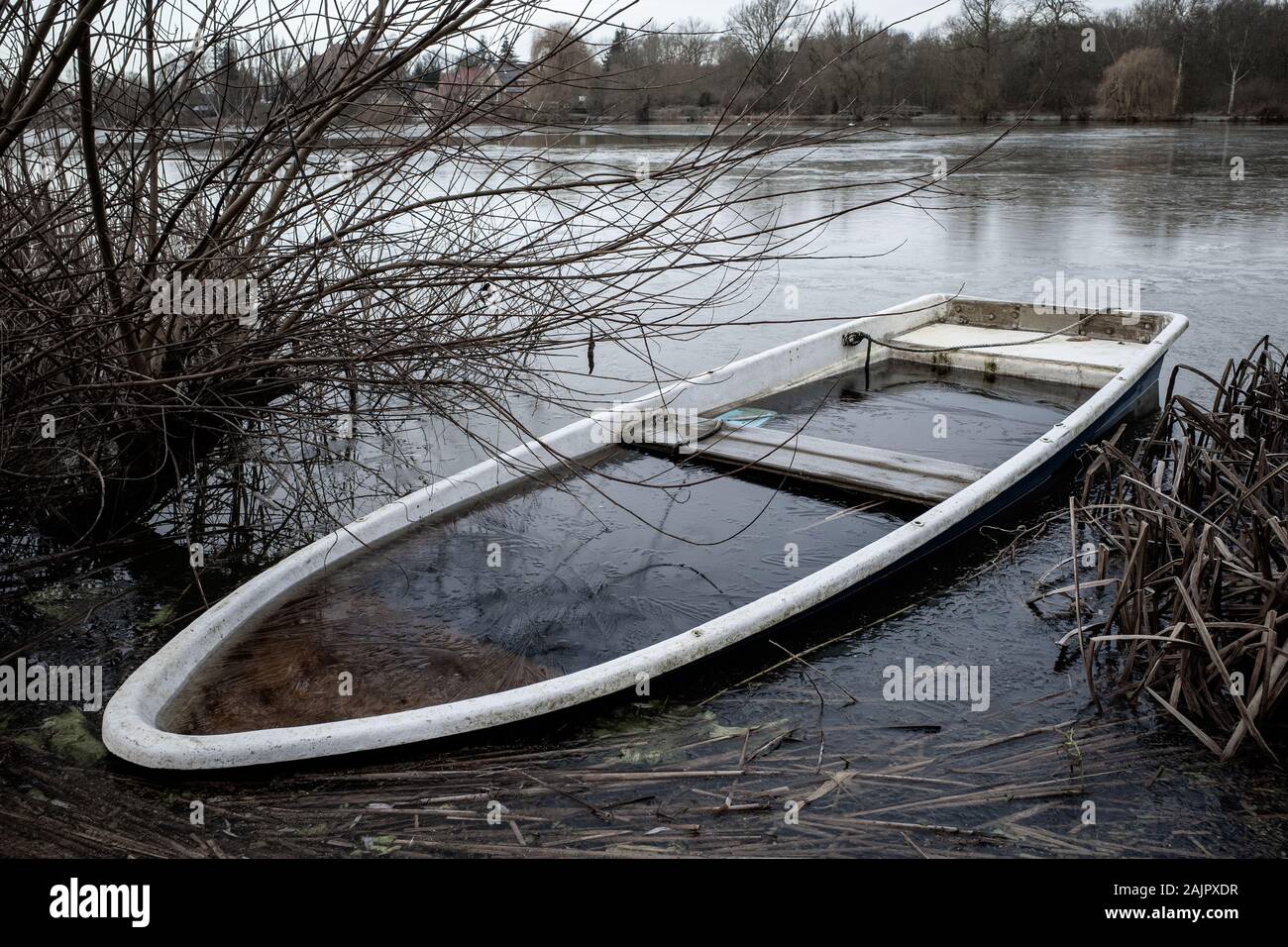 a sunken rowing boat lies on the shore of a frozen small lake Stock Photo