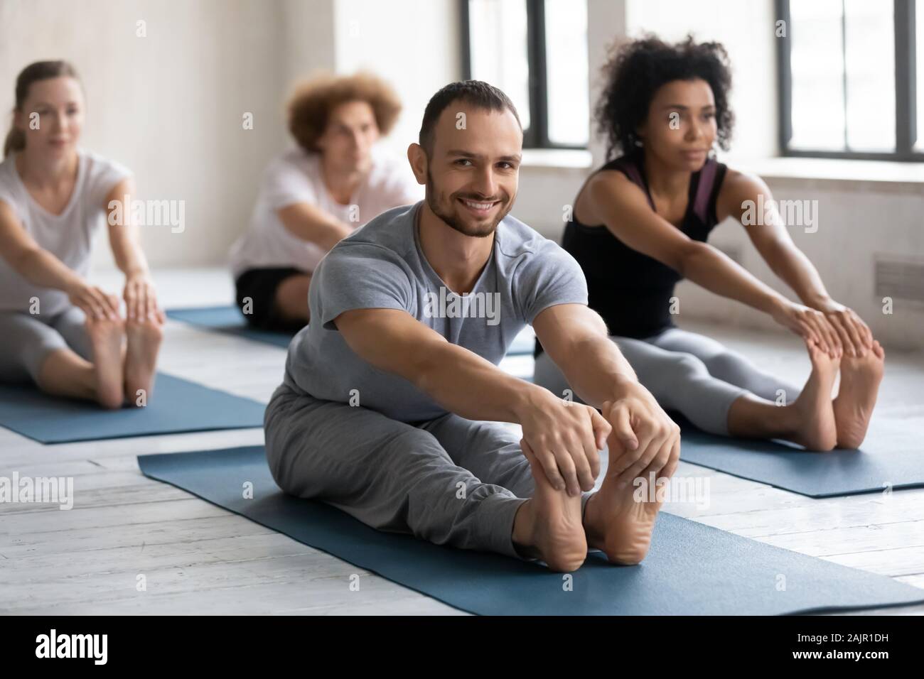 Smiling man practicing yoga at group lesson, Seated forward bend Stock Photo