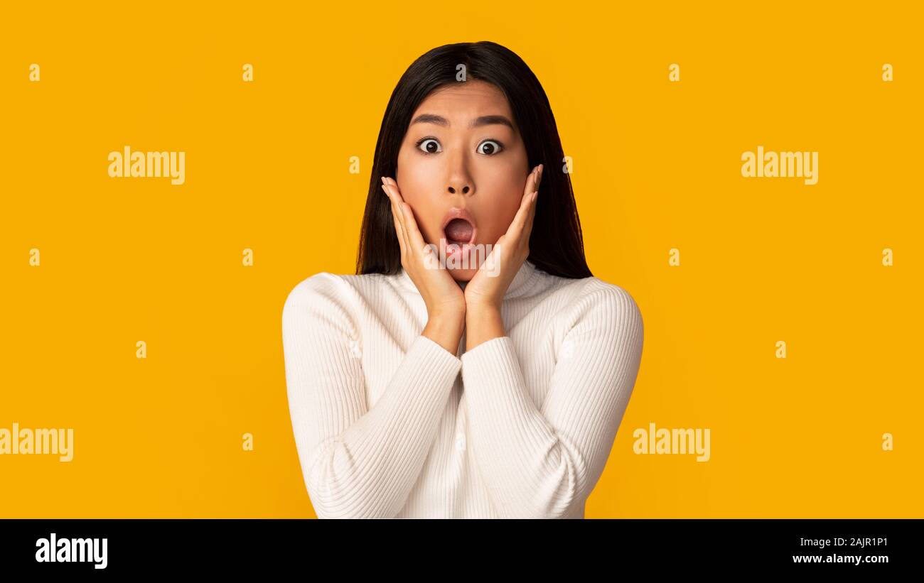 Unbelievable Shocked Asian Girl With Open Mouth And Hands On Cheeks Over Yellow Background Stock Photo Alamy