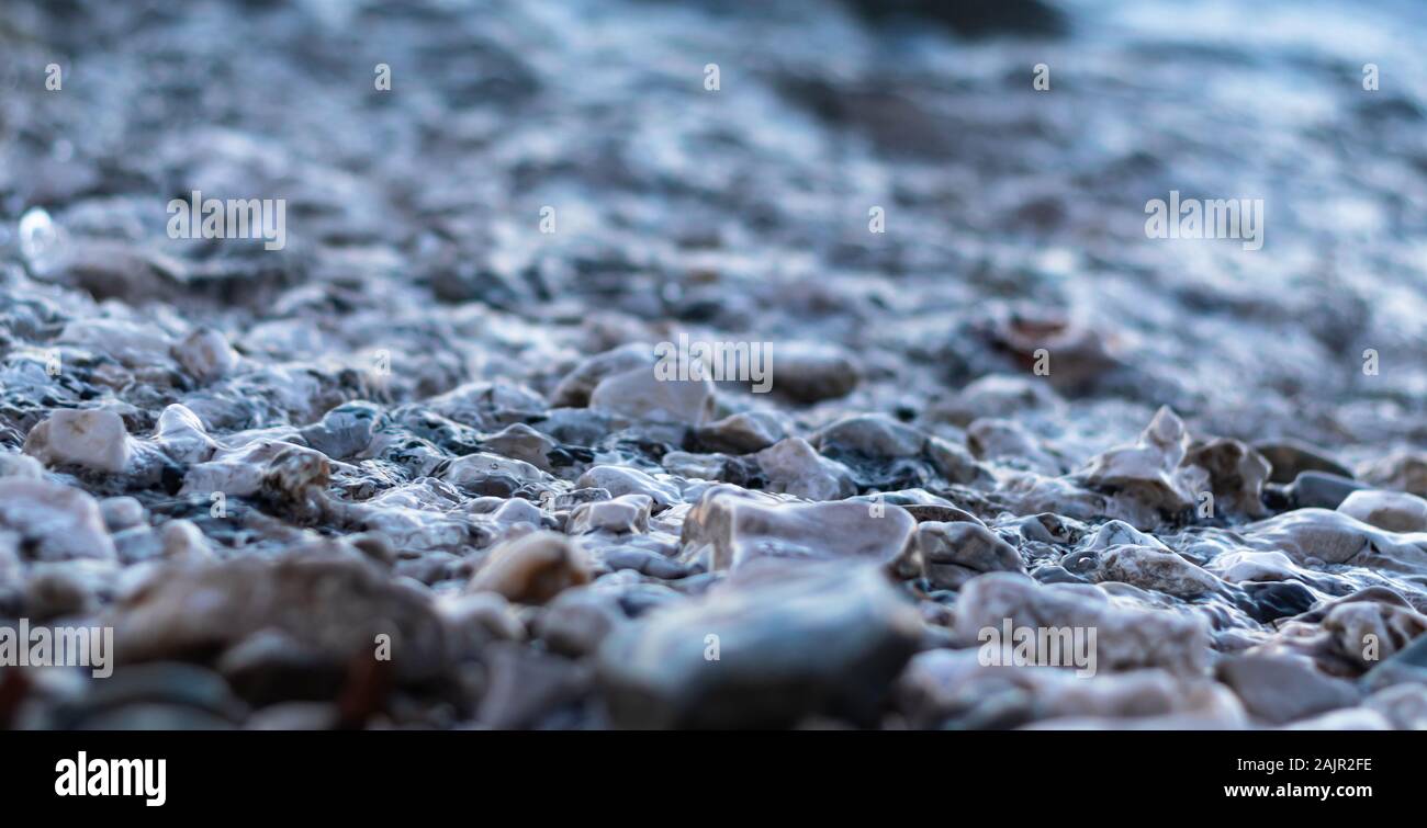 Gravel pebbles at the beach shore, cold photo. Wet stones reflecting sunlight , many different colors of round pebbles Stock Photo