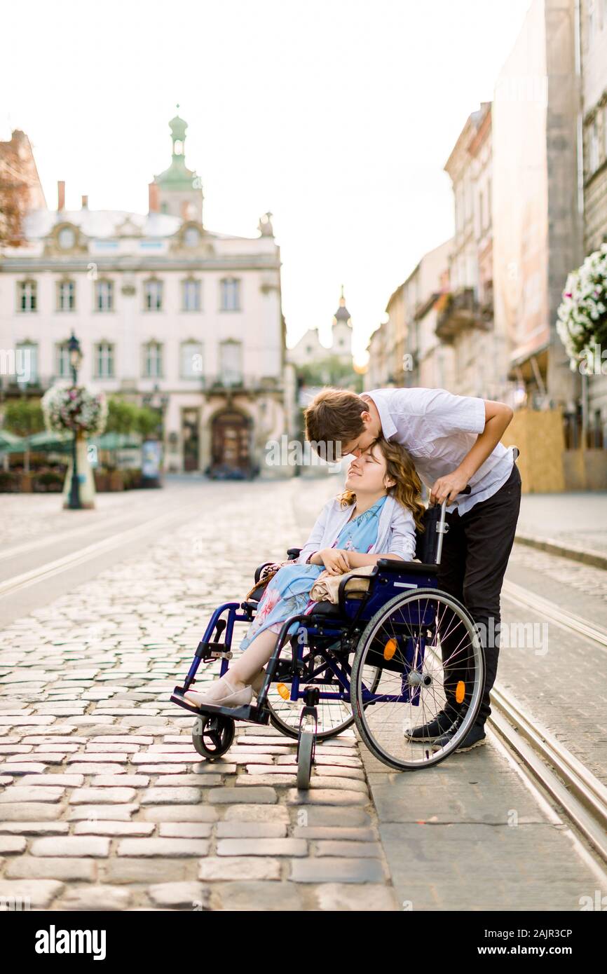 Happy young woman in wheelchair and her husband kissing her forehead