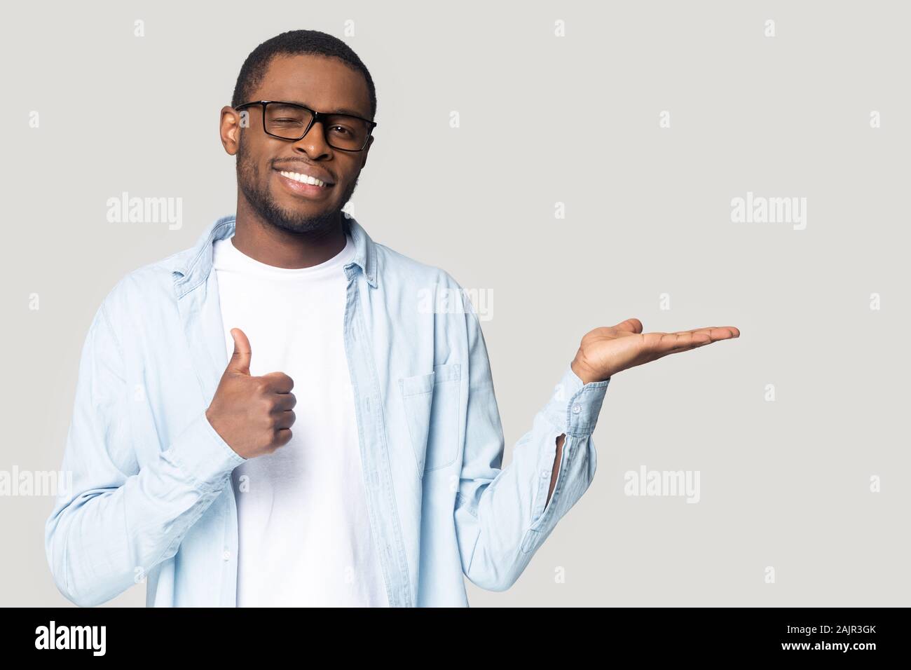 Attractive african guy showing open palm and thumbs up gesture Stock Photo