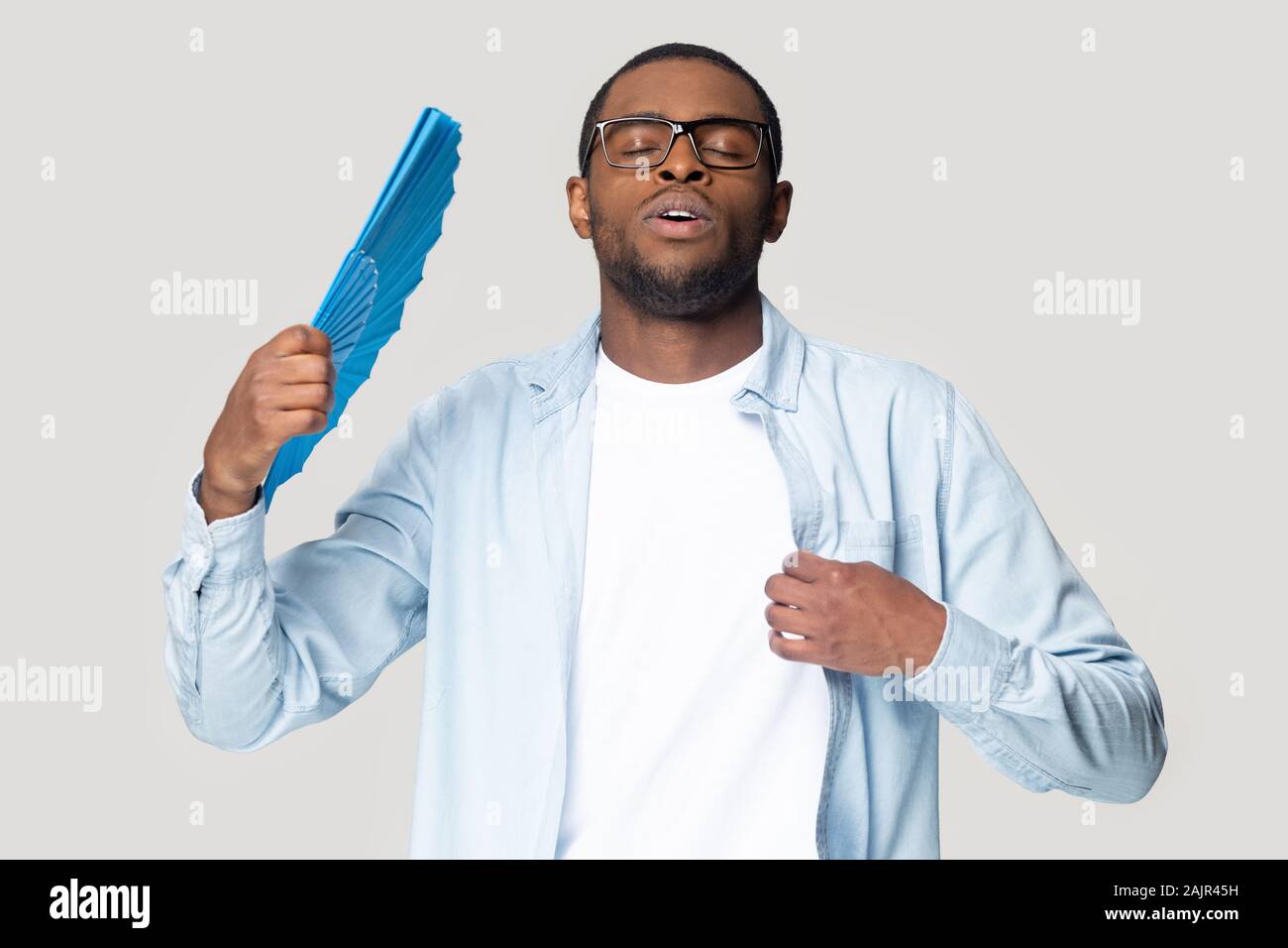 African guy waving fan cooling in hot weather studio shot Stock Photo