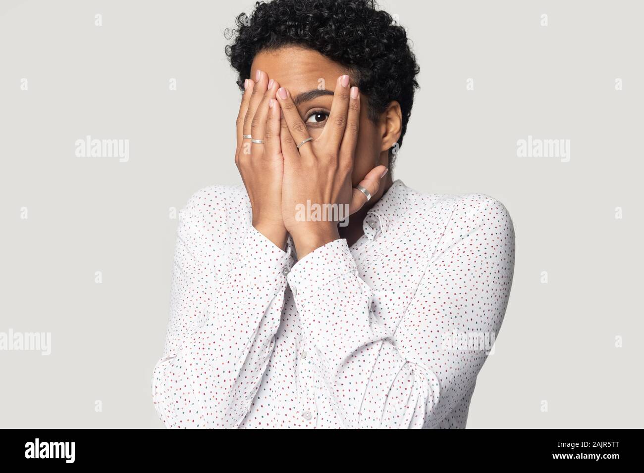 Afraid african woman hiding face with hands peeping through fingers Stock Photo