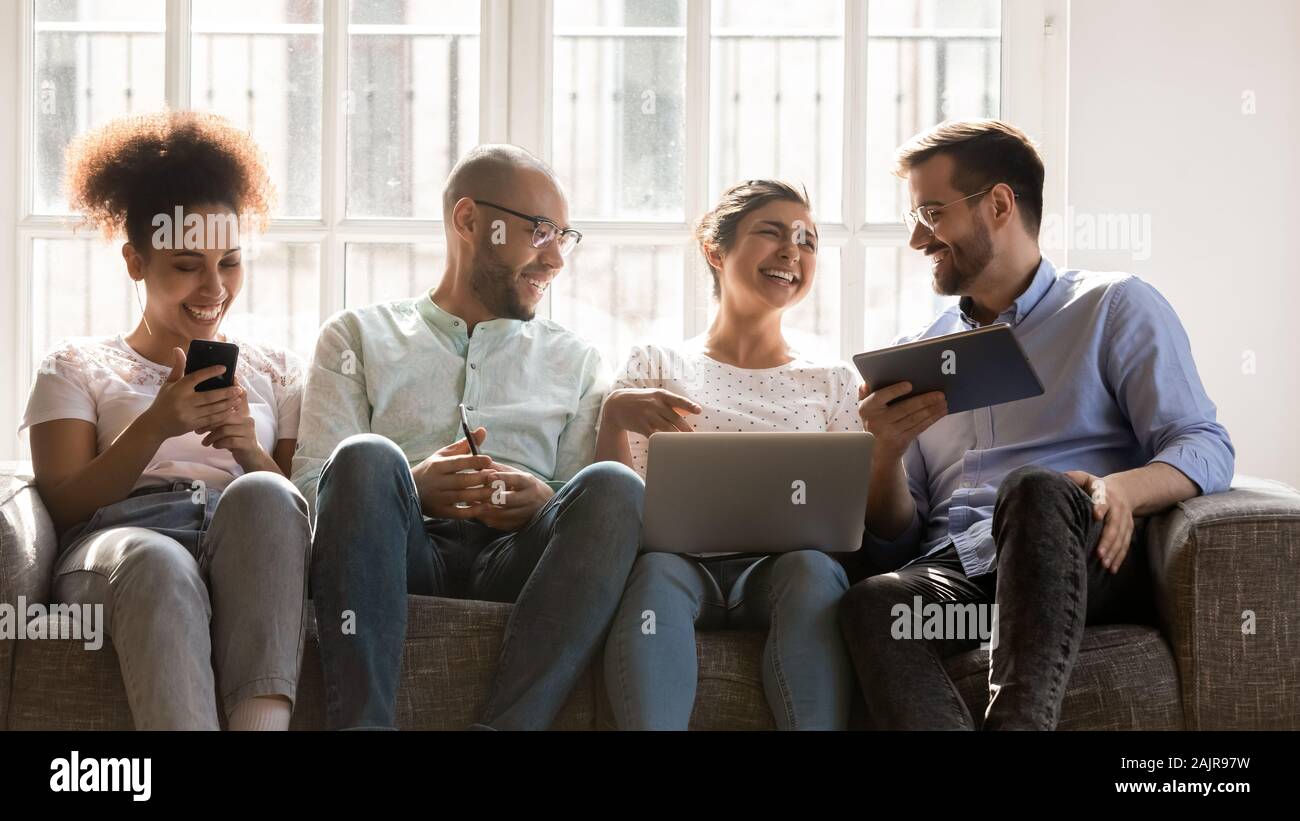 Happy young people sit on couch using modern electronic devices Stock Photo
