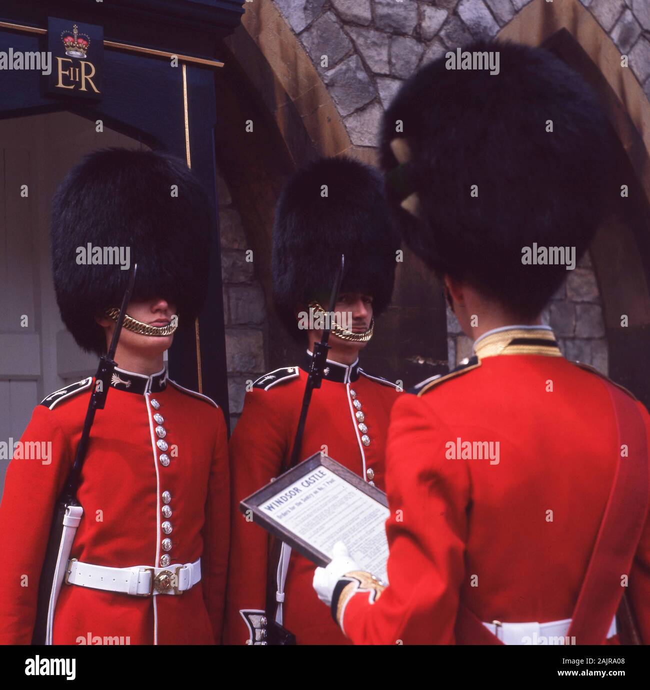 1960s, historical, uniformed Queen's Guard wearing their bearskin hats and red tunics, standing at their Sentry posts, being addressed by their officer at the ceremonial most Noble Order of the Garter, held at Windsor Castle, Windsor, England, UK. The noble of the garter is an order of chivalry founded by Kind Edward III in 1348. Stock Photo