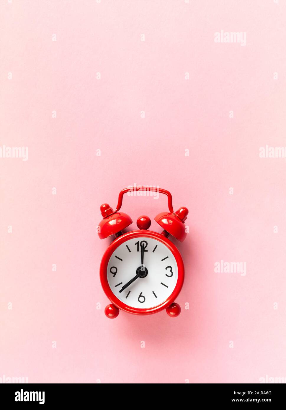 Red small alarm clock on pastel pink background with copy space, flat lay, macro. Minimalism style. Time management, countdown concept. Vertical orien Stock Photo