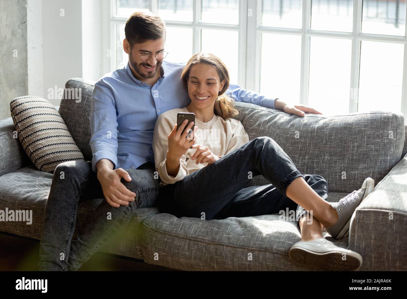 Happy millennial couple relax on couch using cellphone Stock Photo