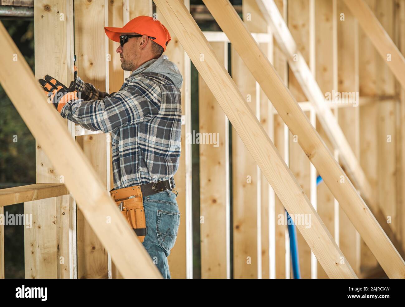 Caucasian Contractor Worker in His 30s with Drill Driver Attaching Wooden Frame Elements. Industrial Theme. Wood House Frame Construction Stock Photo