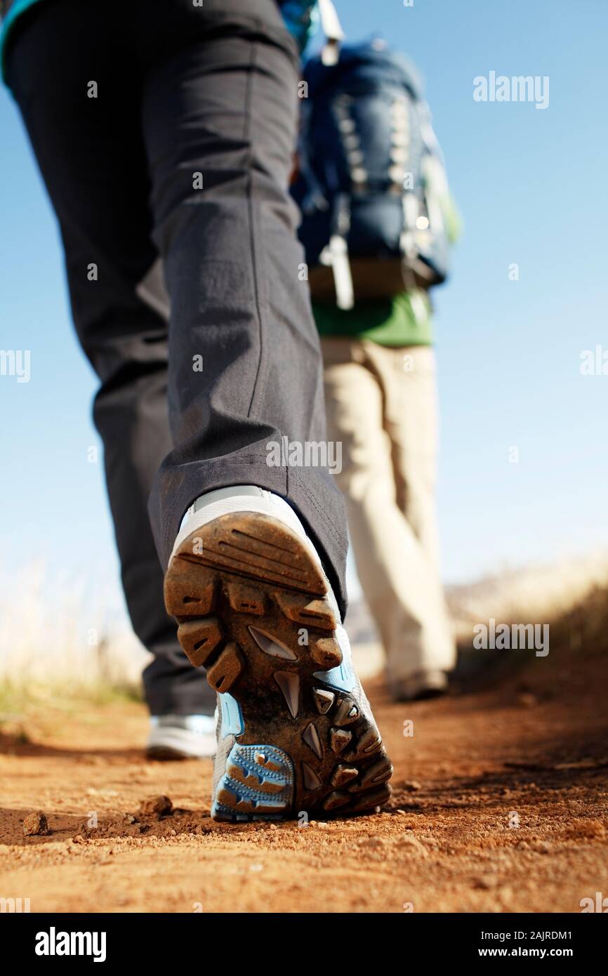 Low closeup of woman's hiking shoe sole as she walks down trail Stock