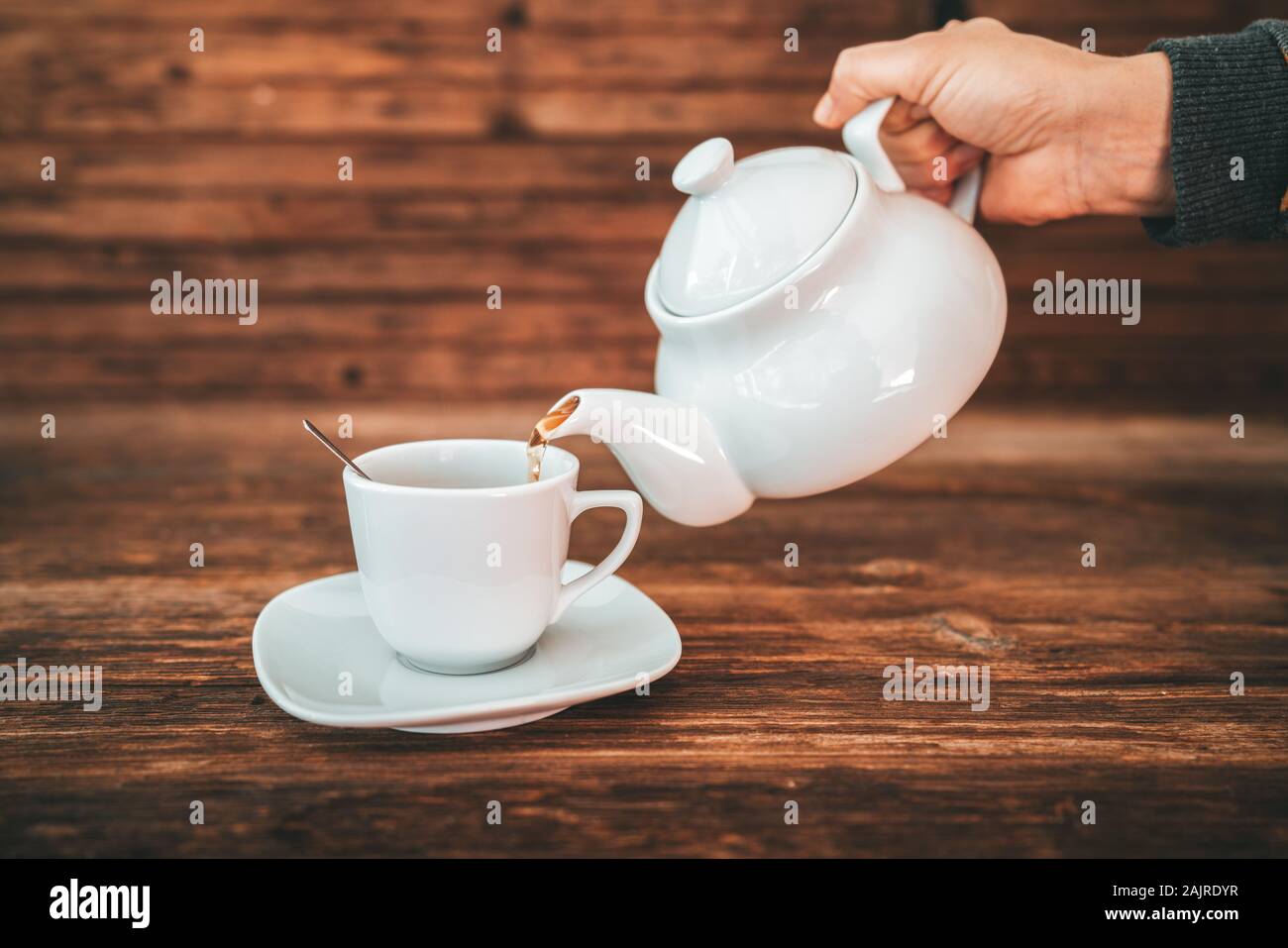 Tea time, brewing and pouring tea, cup of freshly brewed tea, warm soft and light, with wooden background. Stock Photo