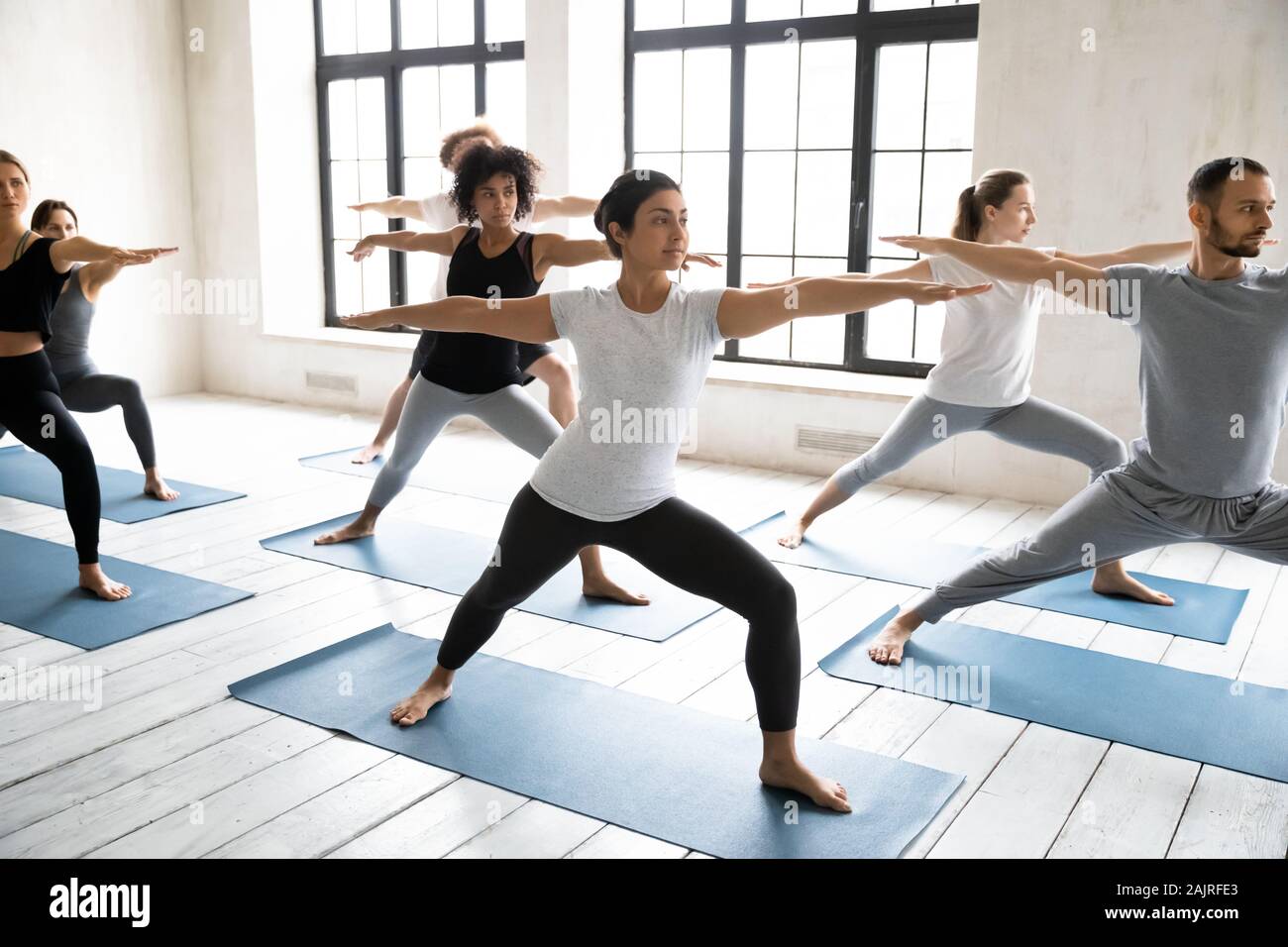 Diverse young people doing Virabhadrasan exercise, practicing yoga Stock Photo