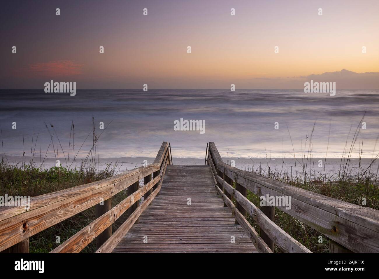A wood pedestrian bridge, built over a sand dune that is used to give beach access in Daytona Beach, Florida, glows during a morning sunrise. Stock Photo
