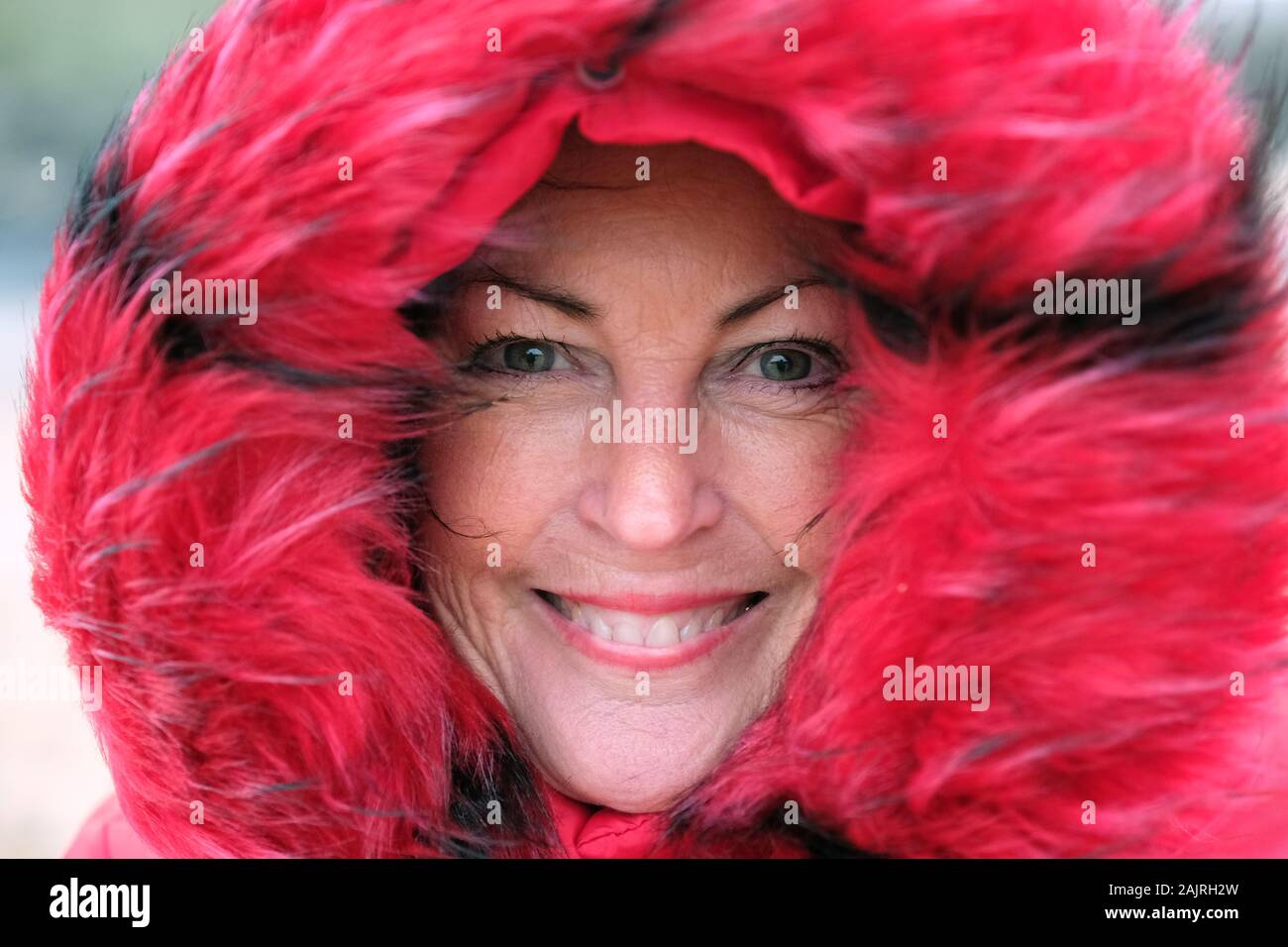 Close-up of a mature, beautiful woman in a red, fur-lined parka - John Gollop Stock Photo